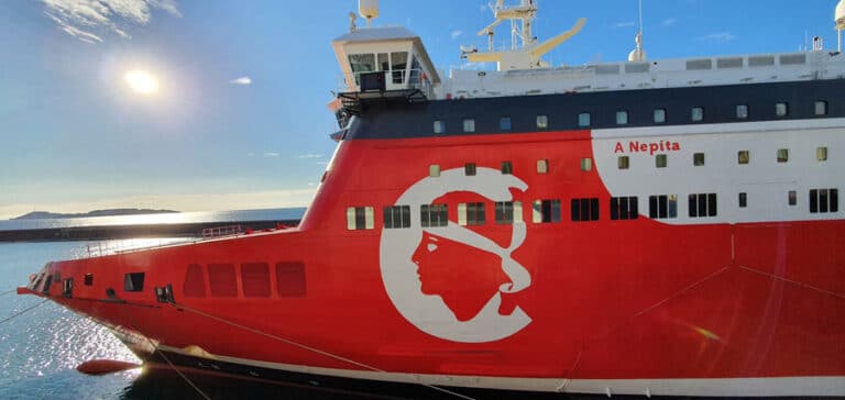 A close-up of the bow of a red passenger ship with white details from the side