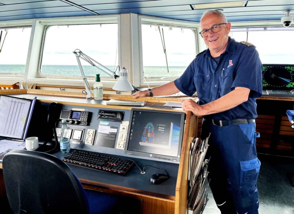 Una foto de Allan Hjortnæs Pedersen, Jefe de Mantenimiento del Læsøfærgen, de pie en el puente del buque, junto al pupitre de mando.