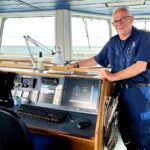 Una foto de Allan Hjortnæs Pedersen, Jefe de Mantenimiento del Læsøfærgen, de pie en el puente del buque, junto al pupitre de mando.