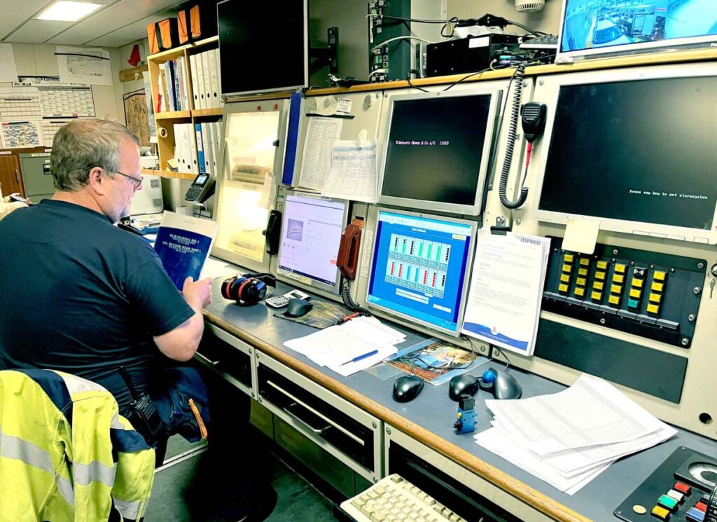 A picture of a maritime worker at Læsøfærgen sitting at a desk with multipule screens and controls