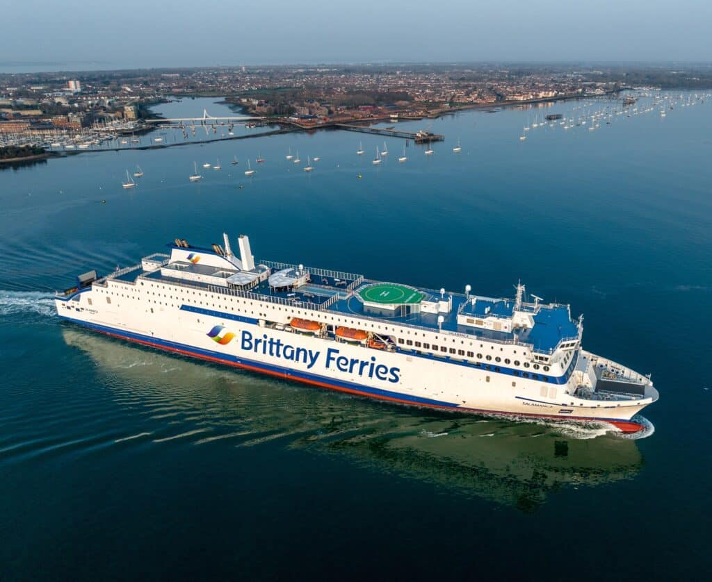 A wideshot of Brittany Ferries sailing from land with the land still visible close in the background