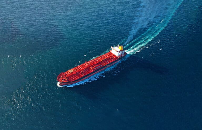 An overview of a tanker vessel at sea sailing full speed across the picture