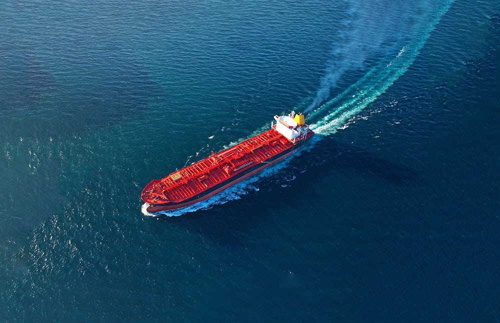 An overview of a tanker vessel at sea sailing full speed across the picture