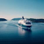 Un barco de pasajeros de DFDS navega por una estrecha vía navegable rodeada de colinas boscosas bajo un cielo despejado