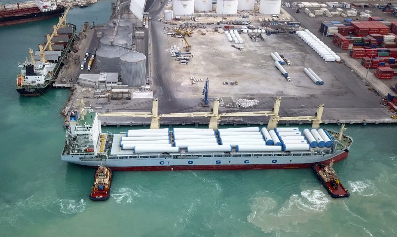 A photo of a maritime vessel being assisted in docking by two tugboats