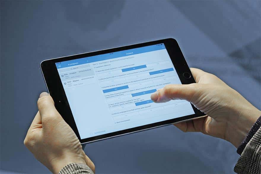 A picture of a tablet with the SERTICA app on the screen is being held by a pair of hans