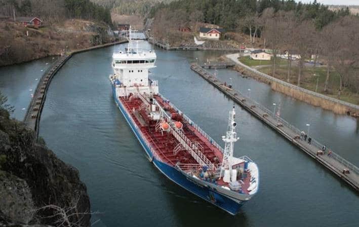 Un gran barco navega por un canal estrecho, rodeado de una exuberante vegetación y aguas tranquilas