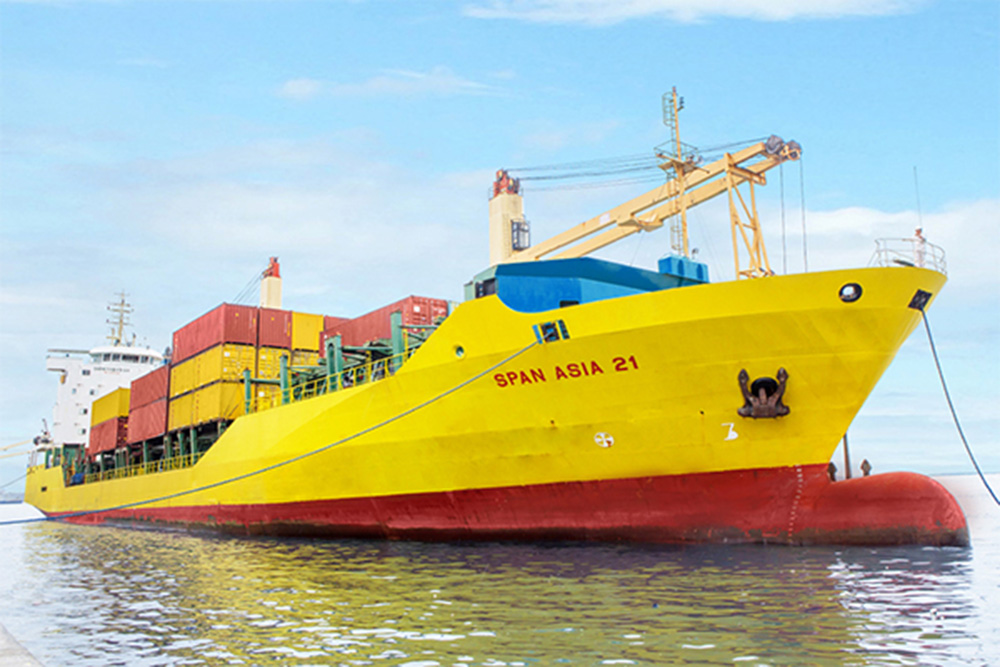 A yellow and red tanker vessel with stacks of colorful containers stacked in rows docking
