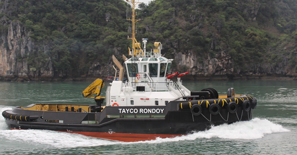 A sideview of a tugboat sailing close to land with mountaints in the background