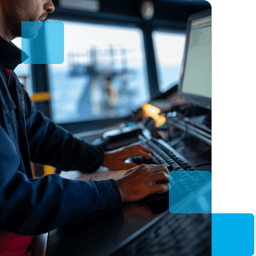 A man in the bridge of the ship working at his computer with the vessel reporting system